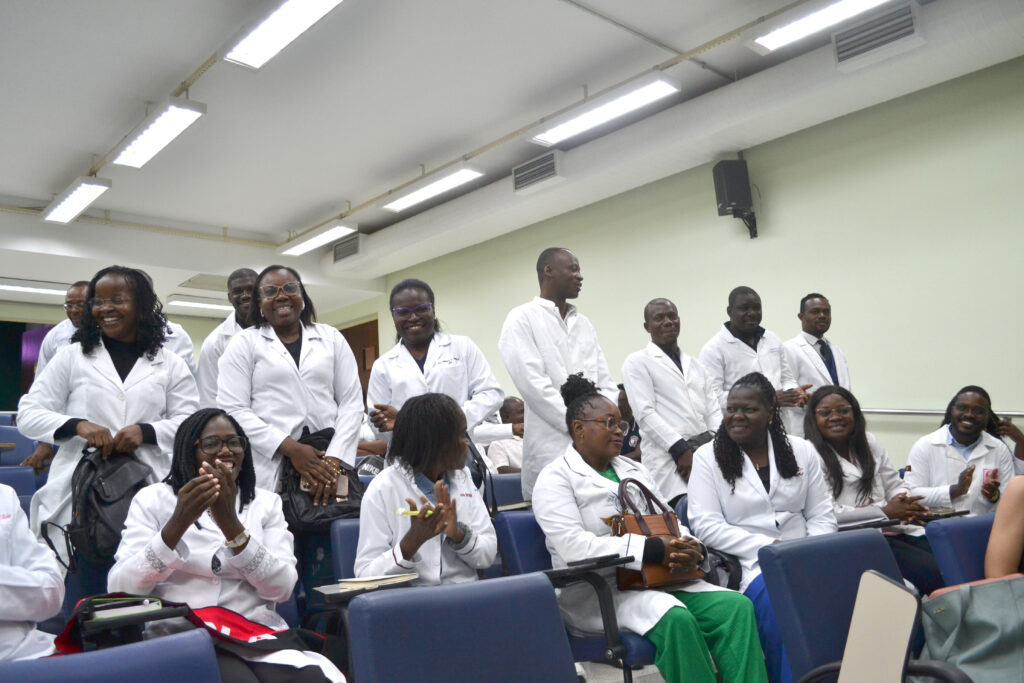Grupo de estudantes em jalecos brancos em sala de aula, celebrando e interagindo durante uma atividade acadêmica.