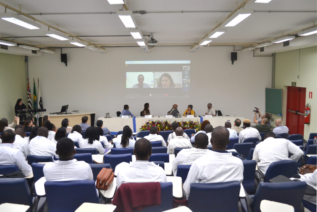 Reunião educacional com diversos participantes, incluindo apresentação virtual em telão e debate sobre temas relevantes.