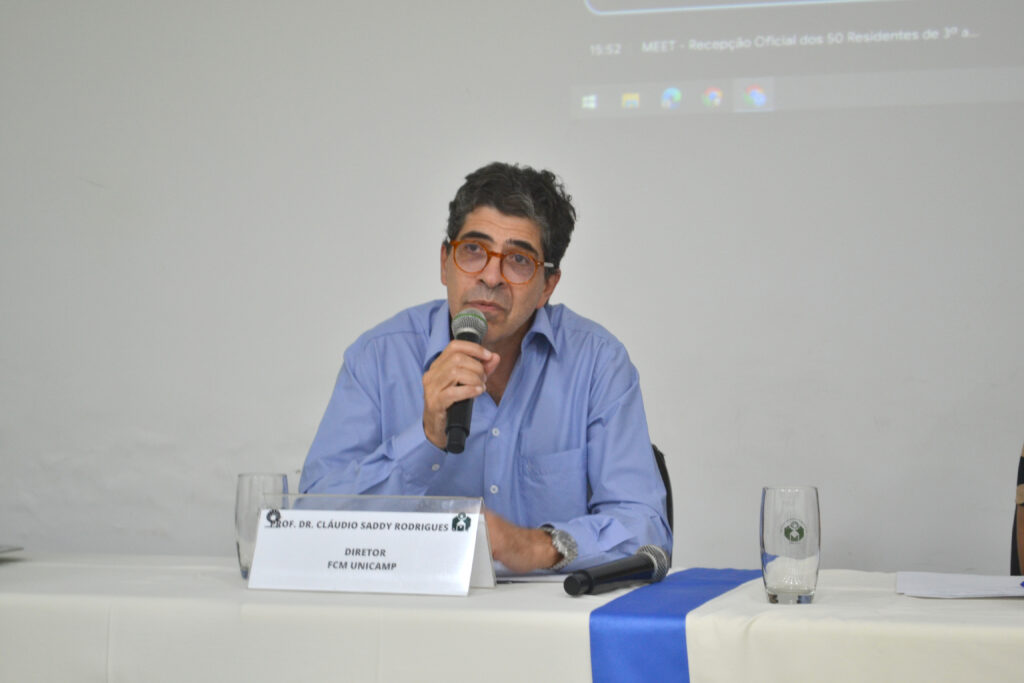 O professor Dr. Claudio Saddy Rodrigues, diretor da FCM Unicamp, participando de uma reunião, segurando um microfone e discursando.