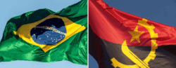 Duas bandeiras nacionais hasteadas contra o céu azul. À esquerda, a bandeira do Brasil, com fundo verde, losango amarelo, círculo azul com estrelas e a faixa branca com a inscrição 'Ordem e Progresso'. À direita, a bandeira de Angola, com duas faixas horizontais — vermelha em cima e preta embaixo — e um emblema amarelo no centro composto por uma estrela, uma engrenagem e um facão cruzado.