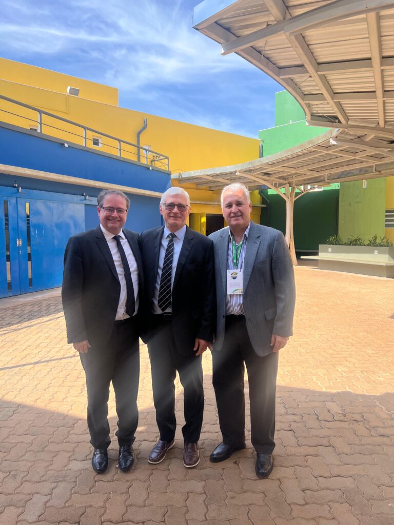 Três professores posam no pátio externo da Faculdade de Ciências Médicas da Unicamp, com prédios coloridos ao fundo. 