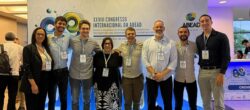 Um grupo de oito pessoas posando em frente ao painel do XXVIII Congresso Internacional da ABEAD. Todos usam crachás de identificação e sorriem para a foto. O painel traz o logotipo da ABEAD e a frase “Rotas e Desafios na Prevenção e Tratamento; Navegando nas Dependências da Contemporaneidade”.