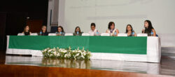 Mesa de abertura da 23ª Semana Acadêmica de Fonoaudiologia da FCM Unicamp, composta por docentes e convidados, posicionada sobre palco com toalha verde e arranjo de flores brancas. Ao fundo, o telão exibe o logotipo do evento e o período de realização, de 22 a 26 de setembro de 2025.