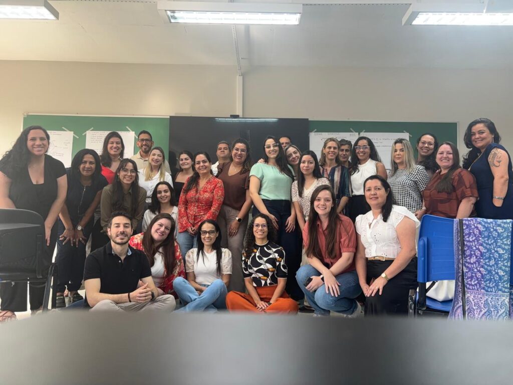 Grupo numeroso de pessoas reunidas para foto coletiva dentro da sala de aula, sorridentes e em pé.