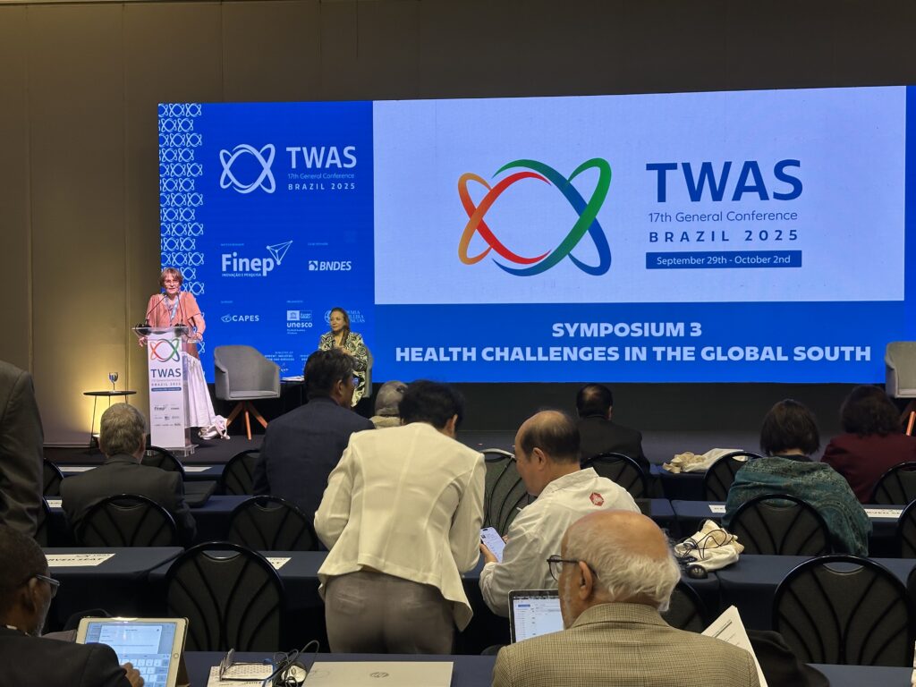 A primeira foto mostra um momento da 17ª Conferência Geral da TWAS, Brasil 2025, que ocorreu de 29 de setembro a 2 de outubro. No palco, à esquerda, a Professora Helena Nader, presidente da Academia Brasileira de Ciências (ABC) e co-organizadora do evento, está de pé em um púlpito, discursando para o público. Atrás dela, uma grande tela exibe o logo da TWAS, o título do evento e a menção ao "SYMPOSIUM 3: HEALTH CHALLENGES IN THE GLOBAL SOUTH" (Simpósio 3: Desafios de Saúde no Sul Global). Uma plateia, composta majoritariamente por pessoas sentadas em mesas com cadeiras de conferência, observa a apresentação, algumas usando notebooks ou tablets.