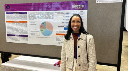 Mulher sorri em frente a um pôster científico fixado em painel cinza durante o congresso ACR Convergence 2025. O pôster, com logotipos da Unicamp e do congresso, tem o título Beyond the Glands: Hypogammaglobulinemia as a Clue to Peripheral Neuropathy in Sjogren’s Disease e exibe um gráfico de setores colorido no centro.