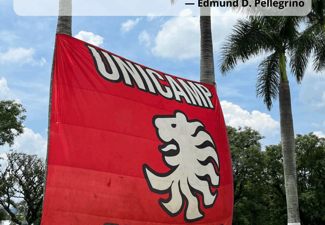 Faixa vermelha com o logotipo da Atlética de Medicina da Unicamp, estendida em área gramada com palmeiras ao fundo. Na imagem, aparece a frase “Dia do Médico – 18 de outubro. A medicina é a mais humana das ciências, a mais empírica das artes e a mais científica das humanidades — Edmund D. Pellegrino”. Na parte inferior estão os logotipos da Faculdade de Ciências Médicas e da Unicamp.