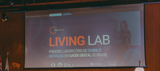 Tela de projeção em auditório exibe o logotipo da SAS Brasil e o título “LIVING LAB – Primeiro laboratório de ensino e inovação em saúde digital do Brasil”. Abaixo, aparecem os logotipos dos parceiros: IOU Unicamp, Philips Foundation e Roche.