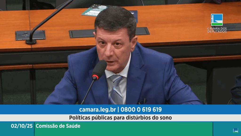 A imagem registra um homem, que parece ser um deputado ou convidado, vestindo terno azul e gravata, falando em um microfone durante uma reunião da Comissão de Saúde na Câmara dos Deputados (cujo logo aparece no canto superior direito), conforme indicado pela legenda na faixa verde. O tema central do debate, claramente exibido na faixa azul, é "Políticas públicas para distúrbios do sono", com a data de 02/10/25 e informações de contato da instituição (camara.leg.br | 0800 0 619 619) dispostas no rodapé da tela.