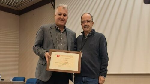 Dois homens segurando um certificado durante o que parece ser uma cerimónia de prémios ou reconhecimento