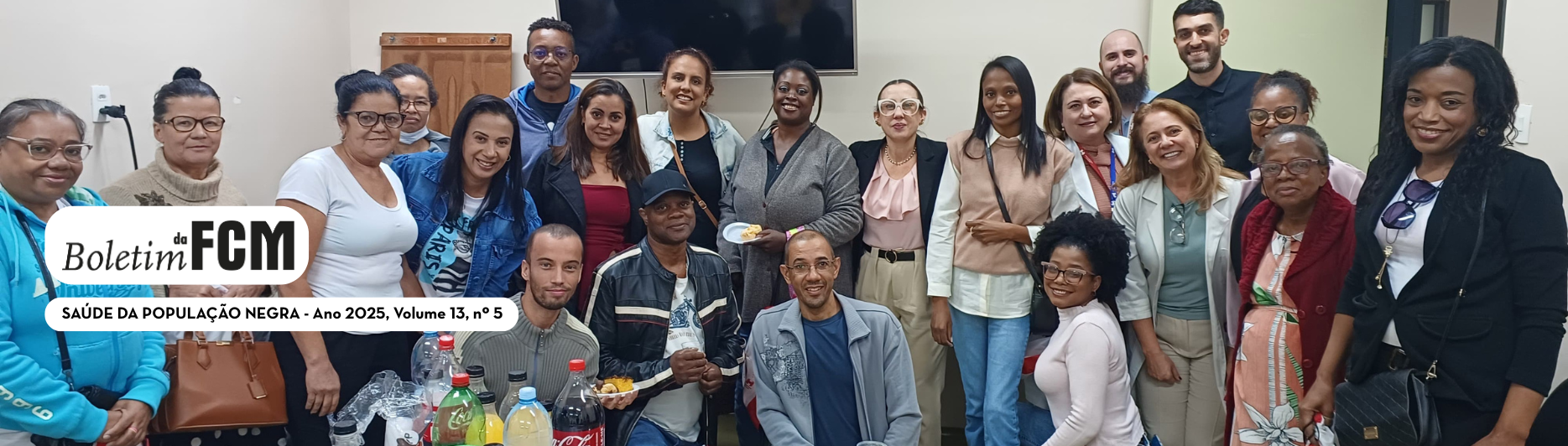 “Grupo numeroso de pessoas reunidas em uma sala, posando para a foto. Estão em pé e sentadas, sorrindo para a câmera. À frente, há uma mesa com garrafas de bebidas e alguns alimentos. No canto esquerdo da imagem, sobreposto, aparece o logotipo ‘Boletim da FCM’ acompanhado do texto ‘Saúde da População Negra – Ano 2025, Volume 13, nº 5’. A cena transmite clima de confraternização e integração.”
