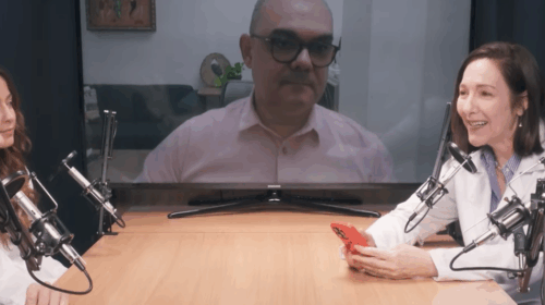 Profissionais da área da saúde participam de uma gravação de podcast em estúdio, sentados ao redor de uma mesa com microfones. Ao fundo, um participante aparece em uma tela, conectado por videoconferência.