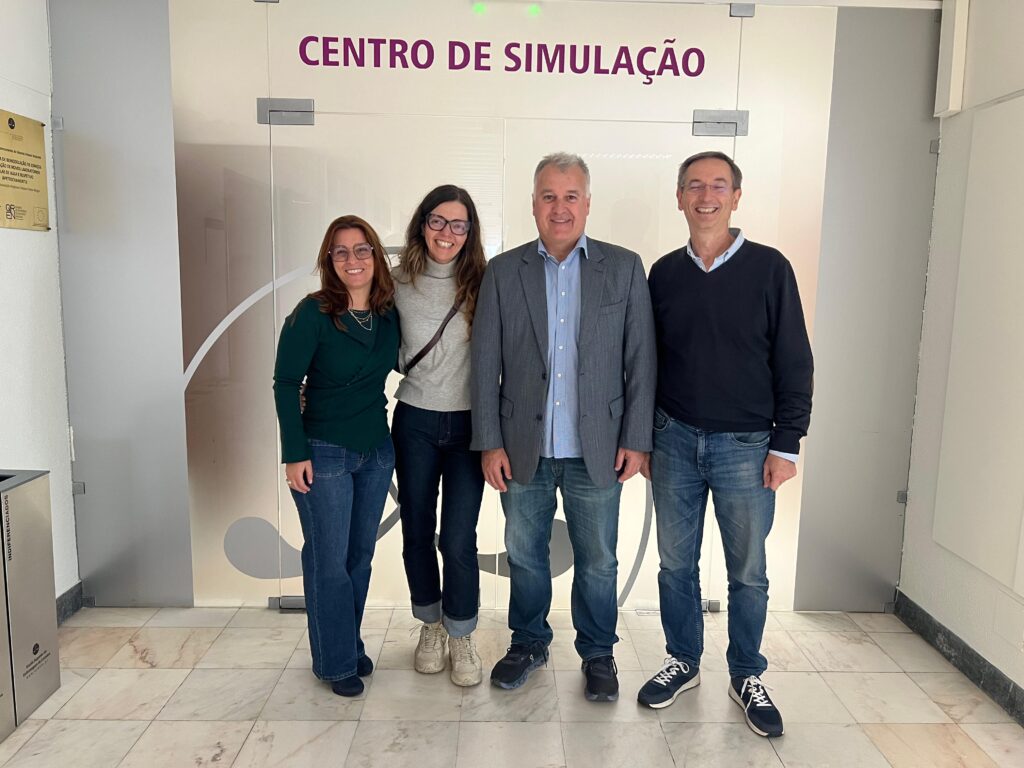 Quatro pessoas posam sorrindo em frente à entrada do Centro de Simulação, em um corredor iluminado. Duas mulheres estão à esquerda e dois homens à direita.