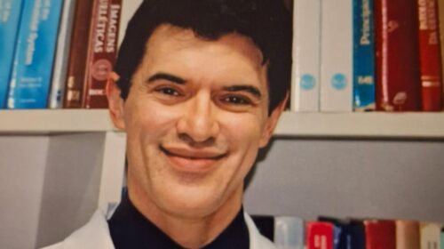 “Retrato do professor Fabiano Reis, docente do Departamento de Radiologia e Oncologia da FCM Unicamp, sorrindo e usando jaleco branco, com uma estante de livros ao fundo.”