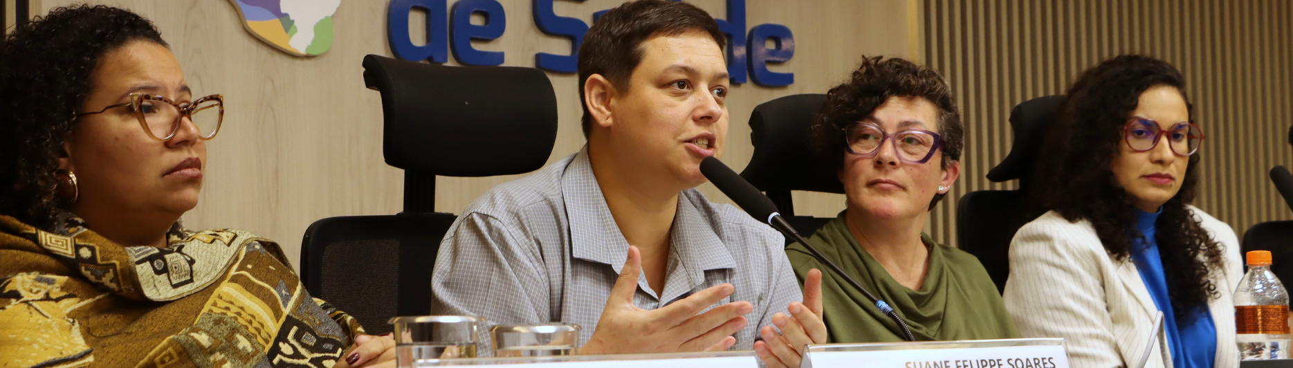 uane Felippe Soares fala ao microfone em mesa de debate ao lado de Michele Seixas.